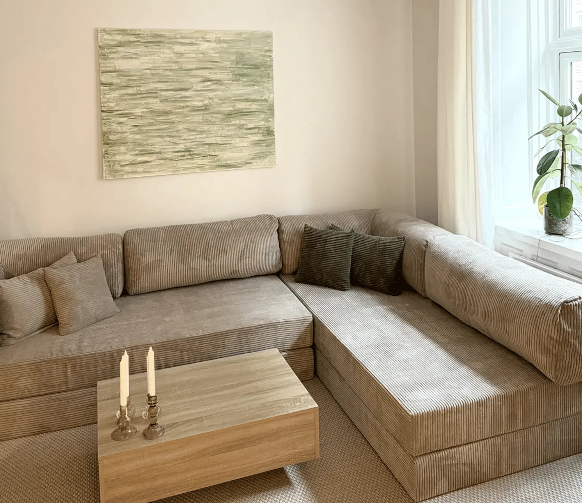 A modern l-shaped sectional sofa in neutral beige ribbed fabric with coordinating throw pillows, displayed in a bright Scandinavian-style showroom setting with natural daylight.