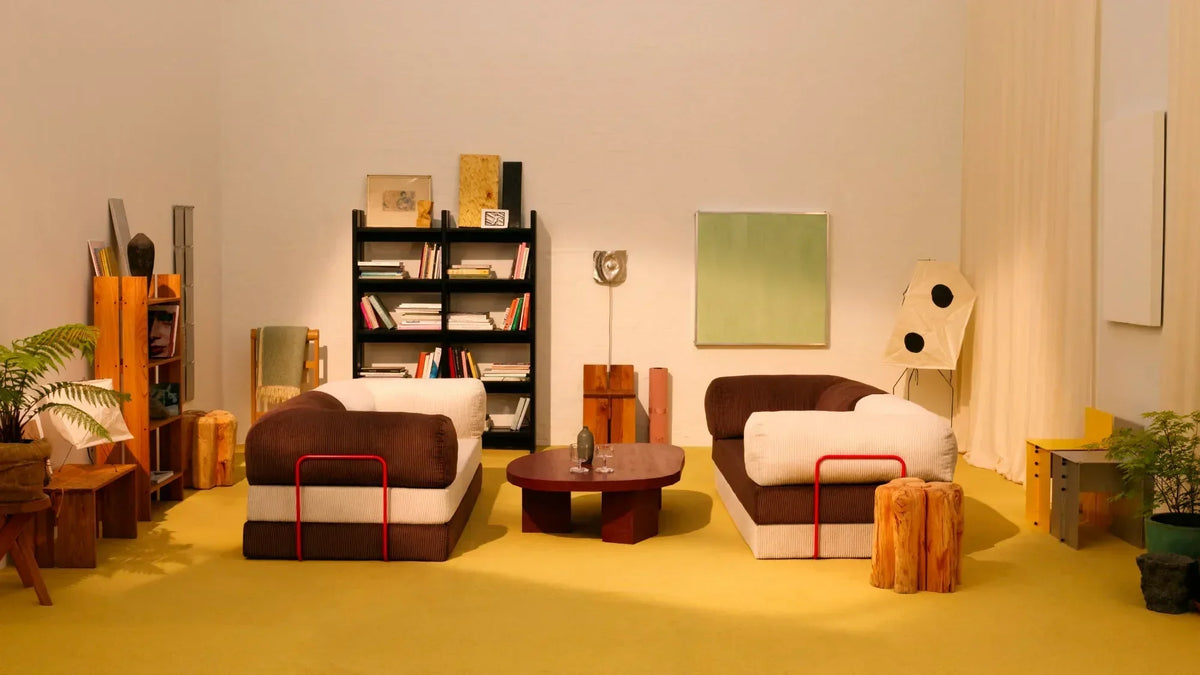 Two contemporary modular sectional sofas with contrasting brown and cream upholstery, arranged in a bright minimalist showroom with bold mustard-yellow flooring and warm beige walls.